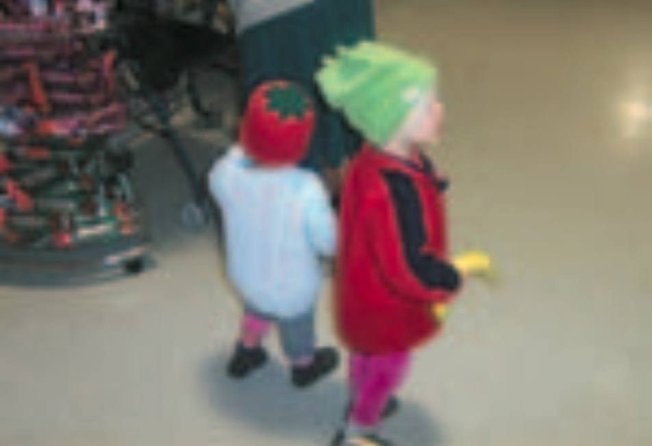Two infants wearing a red beanie and a green beanie in supermarket aisle